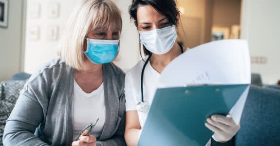 Doctor reviews medical charts with her patient while both wear face masks