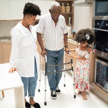 Man assisted at home while using walker to get around in kitchen