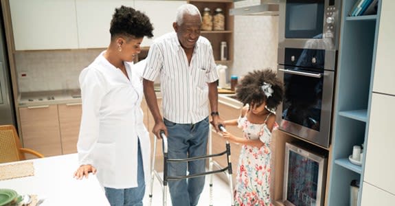 Man assisted at home while using walker to get around in kitchen