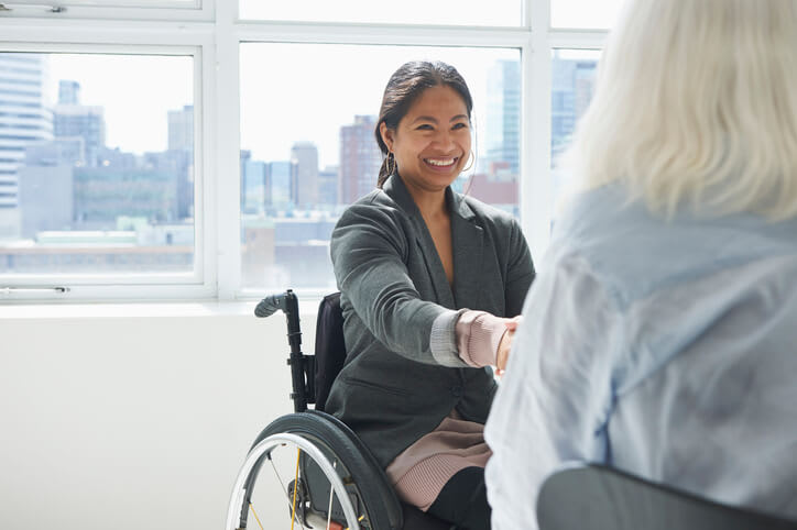 Woman in wheelchair smiles and shakes hands with another woman