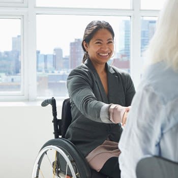 Woman in wheelchair smiles and shakes hands with another woman