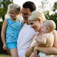 A mother and father hold their young children while standing outside their mobile home