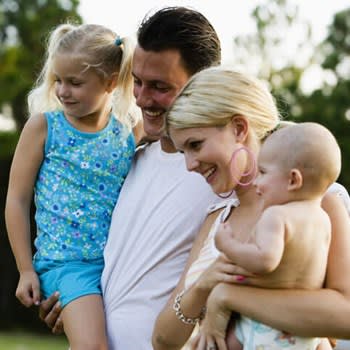 A mother and father hold their young children while standing outside their mobile home