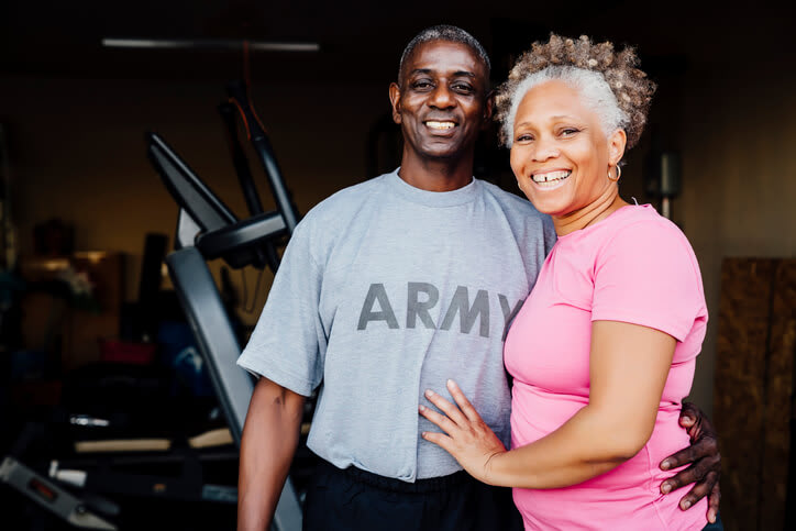 Retired veteran couple smiling in front of home workout equipment