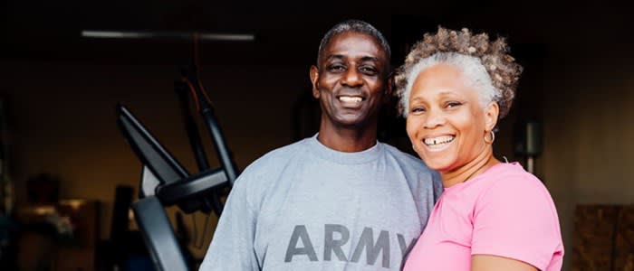 Retired veteran couple smiling in front of home workout equipment