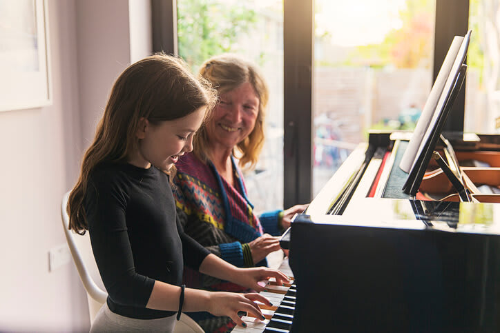 Smiling grandmother teaches granddaughter to play piano