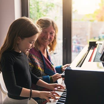 Smiling grandmother teaches granddaughter to play piano