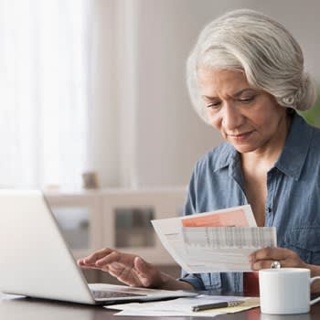 A woman uses her computer while reviewing paper copies of bills