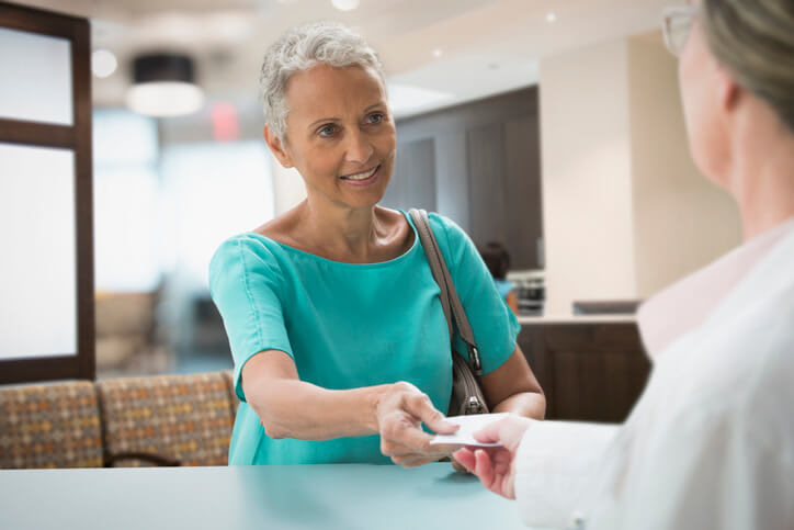 Woman hands her Medicare insurance card to office worker at doctor's office