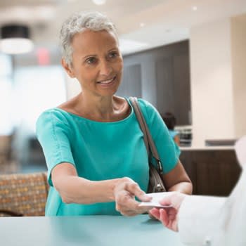 Woman hands her Medicare insurance card to office worker at doctor's office