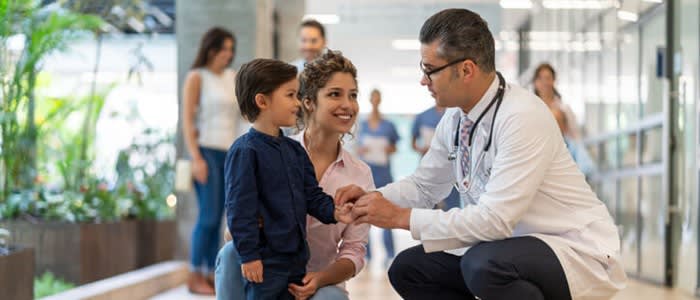 A doctor crouches to speak with young boy and his mother