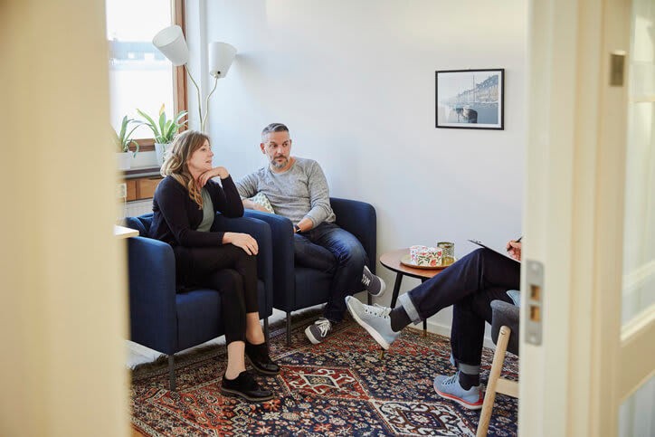 A couple sit on cushioned chairs while speaking with a therapist