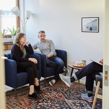 A couple sit on cushioned chairs while speaking with a therapist