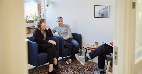 A couple sit on cushioned chairs while speaking with a therapist