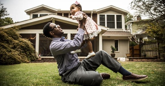 Father holds up his infant daughter while sitting on front lawn