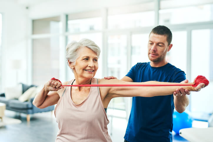 A physical therapist works with a woman while she stretches with exercise bands