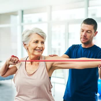 A physical therapist works with a woman while she stretches with exercise bands