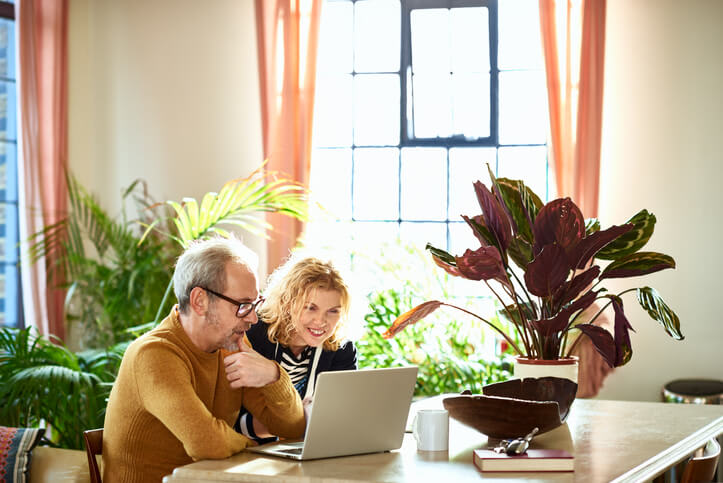 A smiling couple uses their laptop computer in a bright room at home