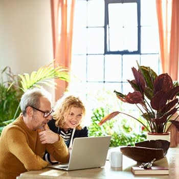 A smiling couple uses their laptop computer in a bright room at home