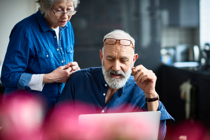 A man uses his home computer while his wife looks over his shoulder