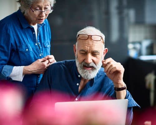 A man uses his home computer while his wife looks over his shoulder