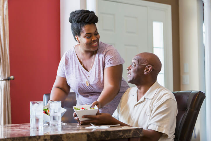 Family caregiver serves lunch to her father