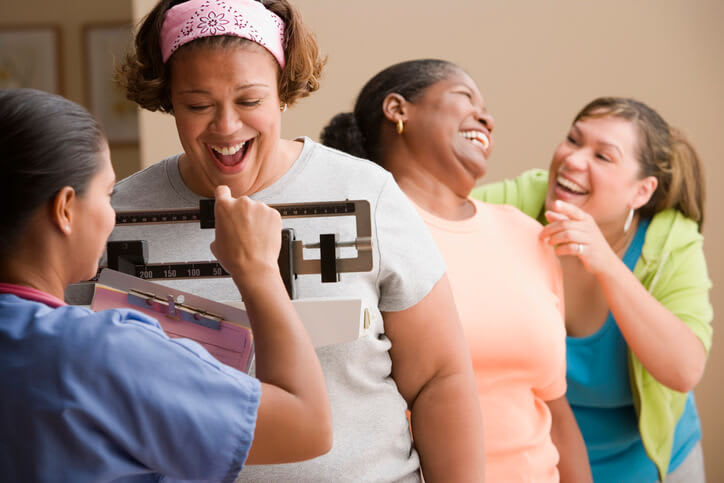 A group of women laugh and celebrate while weighing in for a weight loss group