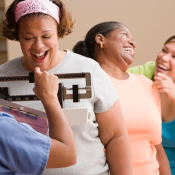 A group of women laugh and celebrate while weighing in for a weight loss group