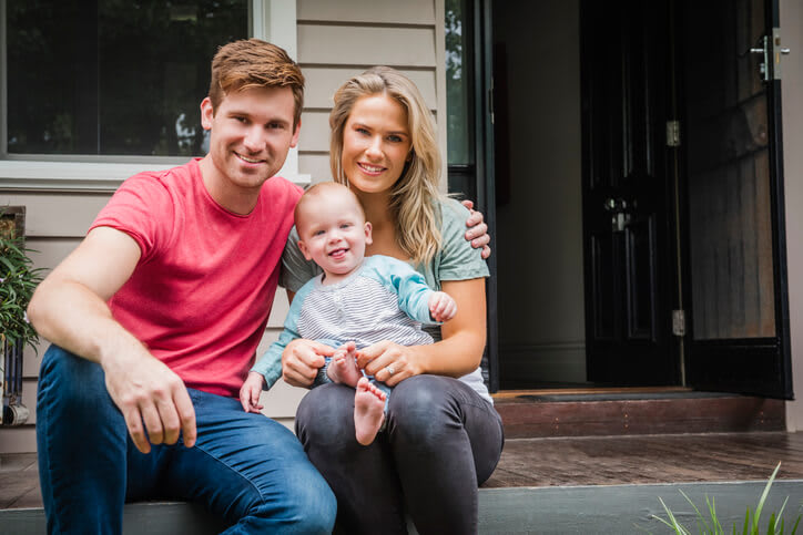 Young mother and father smile with small child on house front steps