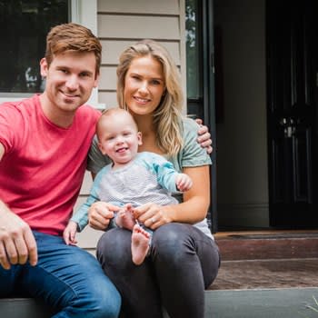 Young mother and father smile with small child on house front steps