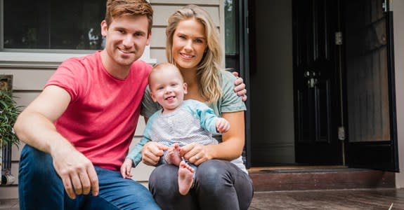 Young mother and father smile with small child on house front steps