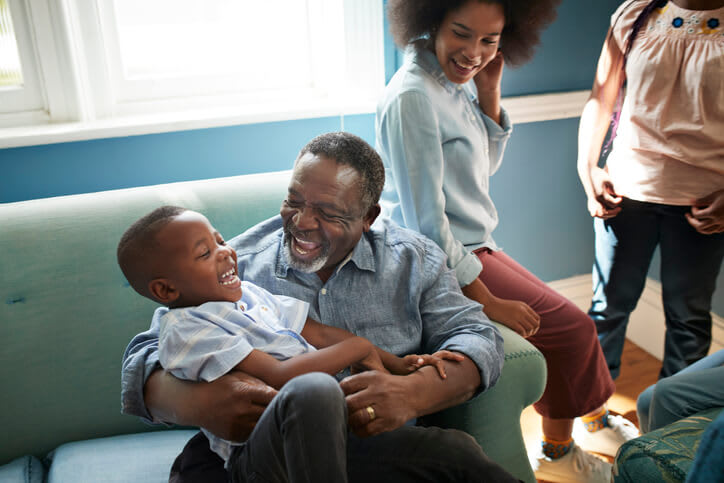 Smiling grandfather plays with young grandson on couch at home