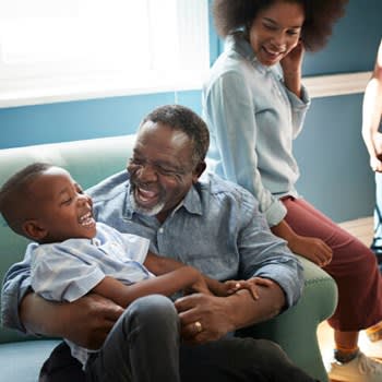 Smiling grandfather plays with young grandson on couch at home