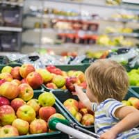 A child reaches for an apple in a grocery store