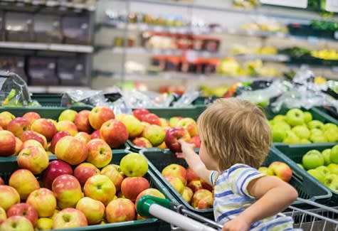 A child reaches for an apple in a grocery store