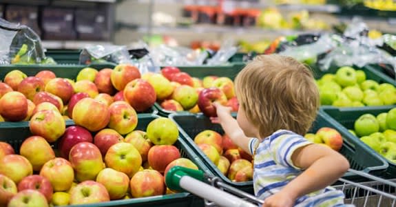 A child reaches for an apple in a grocery store