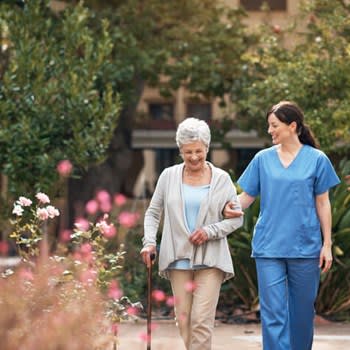 Woman walks in a garden with assistance from caregiver