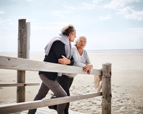 Retired couple leaning on a fence at the beach