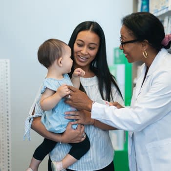 Happy pharmacist speaks with young mother and baby girl