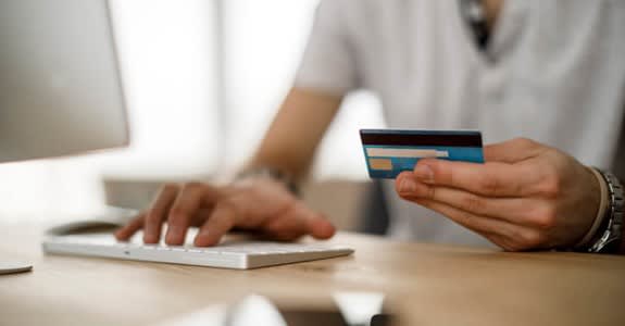 Someone holding credit card while typing on computer