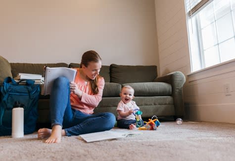 Infant and mother play with toys on living room floor while mother studies