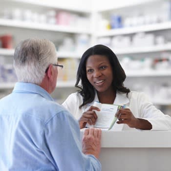 Pharmacist reaches across counter to help patient