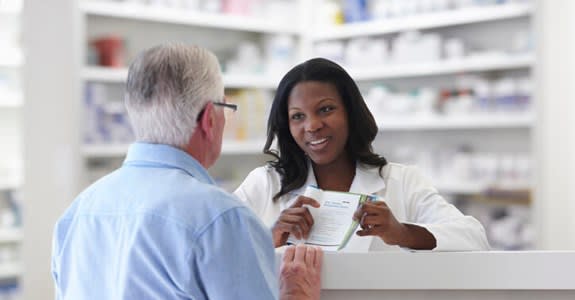 Pharmacist reaches across counter to help patient