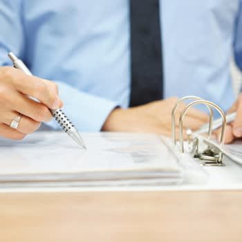 A woman's hand holding a pen points out an item in a binder