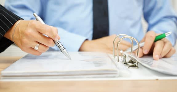 A woman's hand holding a pen points out an item in a binder