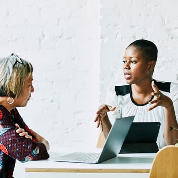 Two women chat while one uses her laptop computer