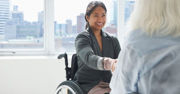 Woman in wheelchair smiles and shakes hands with another woman