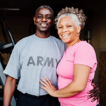 Retired veteran couple smiling in front of home workout equipment