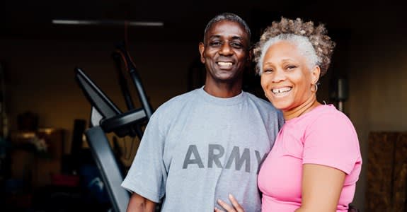 Retired veteran couple smiling in front of home workout equipment