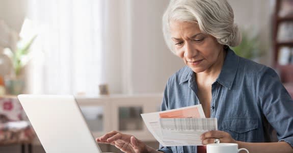 A woman uses her computer while reviewing paper copies of bills